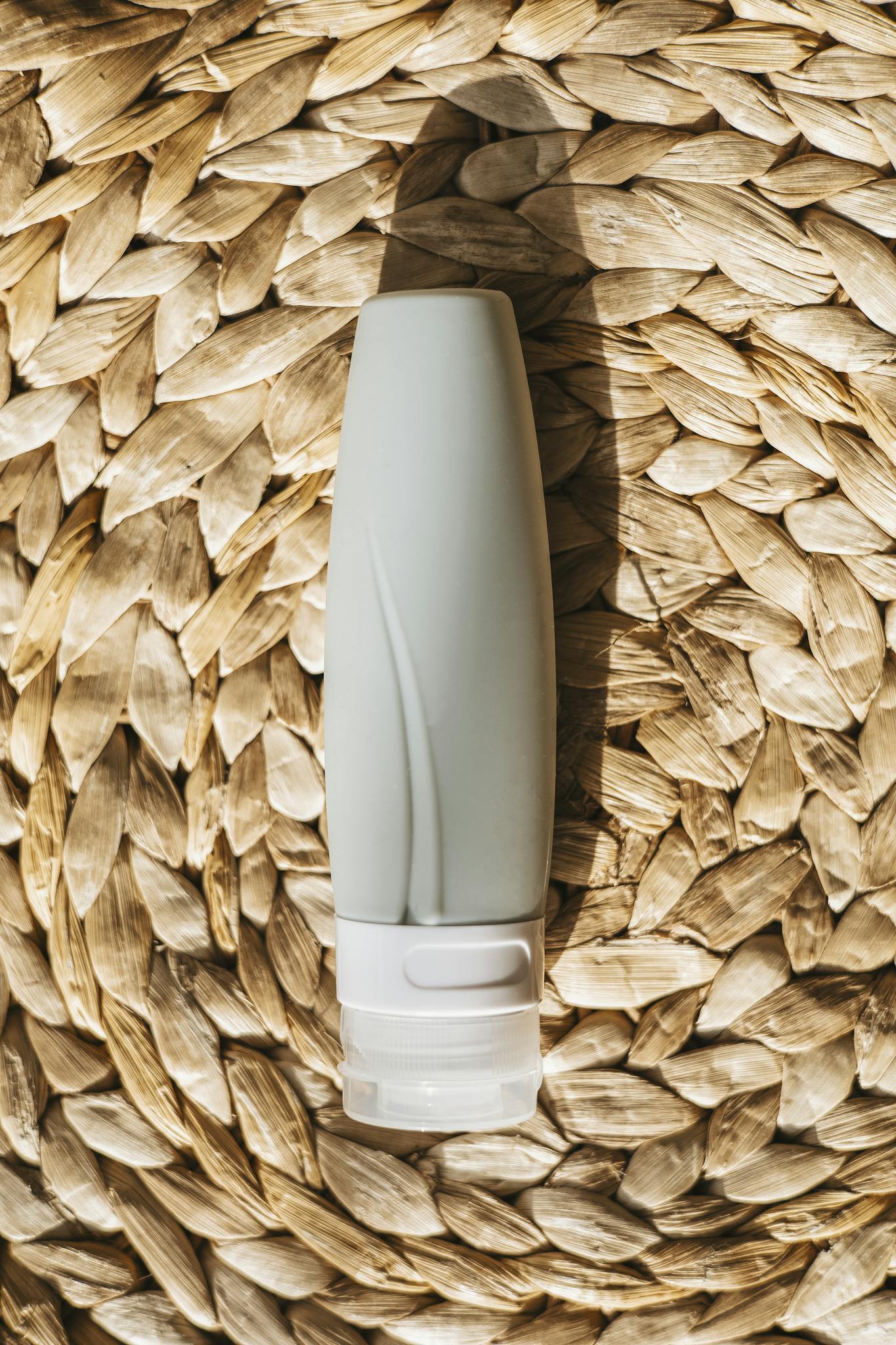 A silicone travel bottle lies on a wicker mat, perfect for travel and toiletries.