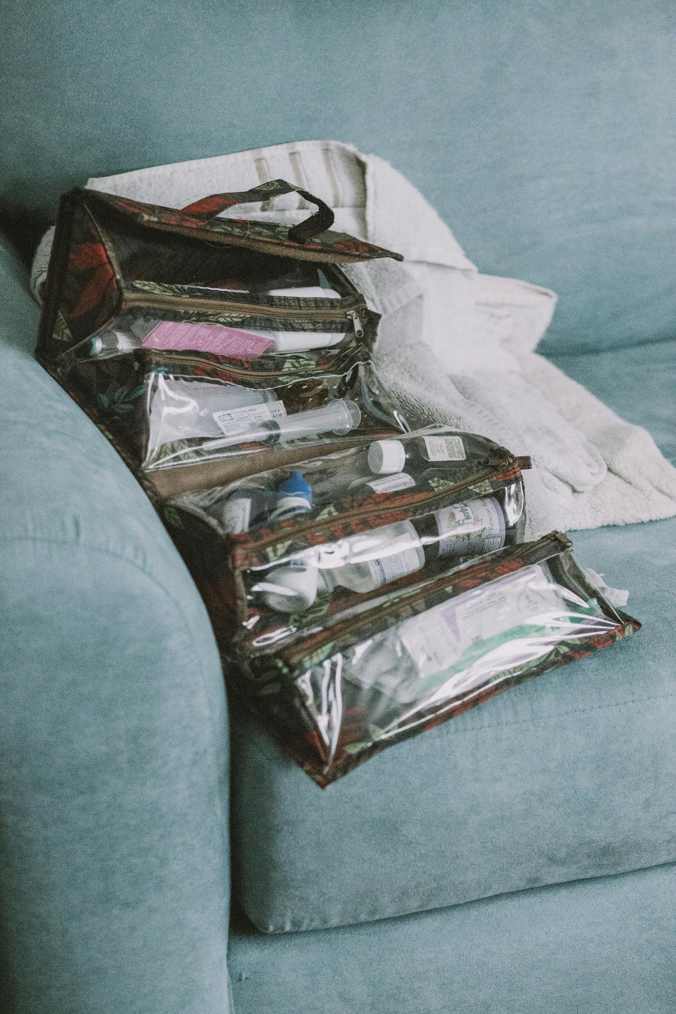 Clear travel bags with toiletries neatly arranged on a teal sofa indoors.
