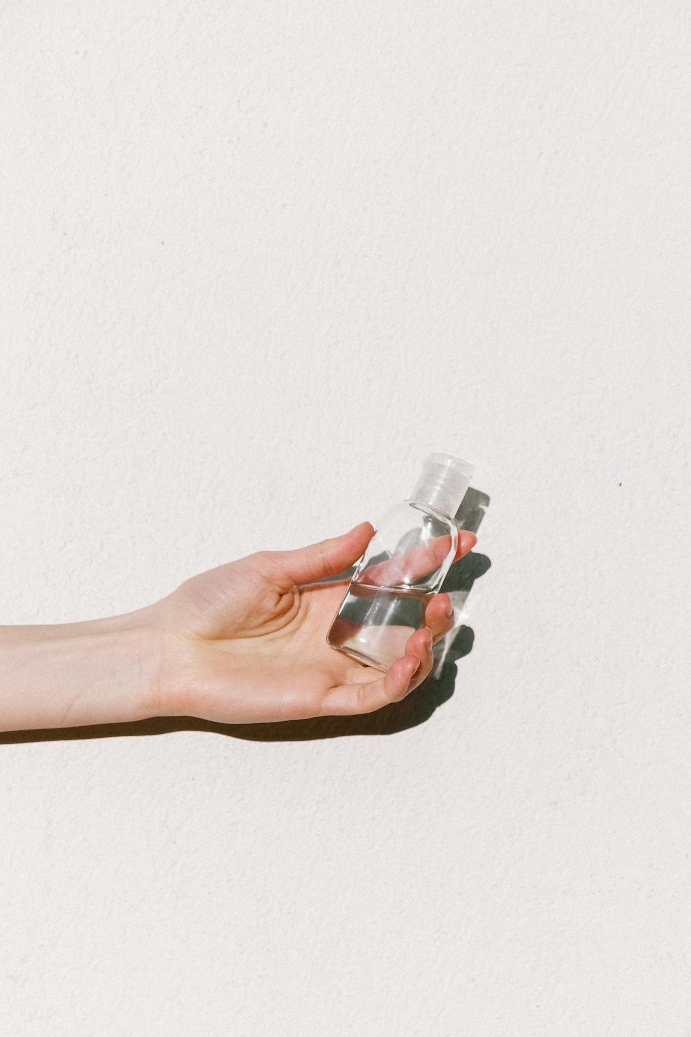 Close-up of a hand holding a transparent sanitizer bottle on a white background.