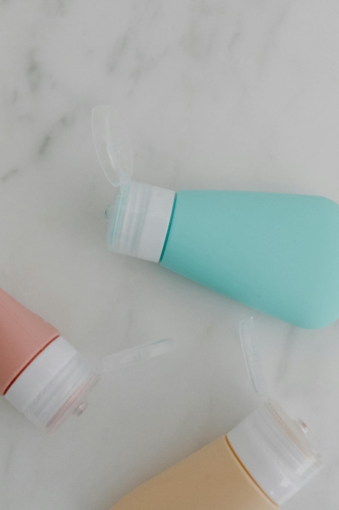 Three pastel-colored fliptop bottles on a marble background, perfect for product mockups.